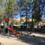 Yacht Swing rocking in vibrant playground with colorful slide and trees in the background.