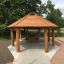 Wooden Long Firehouse gazebo with benches in a park.