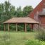 Wooden shelter Long Firehouse in a garden next to a red brick building