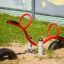 Red SeeSaw playground equipment on sandy ground with a mural in the background.