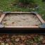 Wooden sandbox for children in a backyard filled with sand and surrounded by autumn leaves
