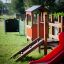 Children's playground equipment with red slide and wooden climbing structure.