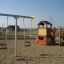 Baby Double Swing in a playground with a playhouse and climbing structure.