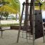 Steel climbing frame on a sandy beach with palm trees in the background.