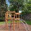 Sherwood wooden playhouse in a park with trees and a stone wall in the background.
