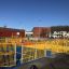 A large outdoor playground structure with multiple yellow metal fences and colorful rubber flooring.