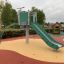 Outdoor playground with the Crow's Nest steel structure featuring a green slide and climbing frame.