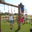 Children playing on Alv playground structure with wooden posts, climbing ropes, and metal arch under