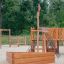 Wooden playhouse outdoor structure with Nature Ship Sandbox in playground setting.