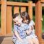 Two children sitting on the wooden Nature Ship Sandbox, wooden playhouse.