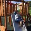 Child playing on Nature Ship Sandbox, wooden playhouse slide.