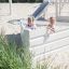Two girls playing in a Nature Ship Sandbox, wooden playhouse on a sandy playground.