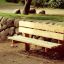 Larchwood Bench placed in a park next to a stone wall.