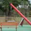 Larchwood Bench in a playground with a swing and slide in the background'