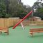 Larchwood Bench in a playground with green flooring and wooden fences.