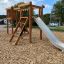 Wooden Alstad playground structure with slide and climbing elements.