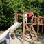 Children playing on an Alstad wooden playground set with a slide and climbing frame.