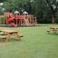 Larchwood Table & Bench in a park with a playground in the background.
