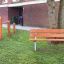 Steel Construction Bench in a park setting with wooden fitness equipment in the background.