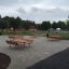 Wooden Table & Bench sets in an outdoor public area with trees and buildings in the background.