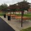 Table & Bench outdoor seating set with wooden tables and benches under a pergola in a park