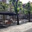 Tables and benches Quadro set under umbrellas on a cobblestone street with trees.
