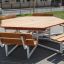 Hexagonal wooden table with six attached benches for outdoor seating.