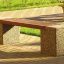 Outdoor park bench Vega with wooden slats and concrete supports on a brick-paved walkway.
