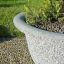 Large Bell stone planter filled with plants on pebble pathway.