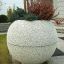 Stone garden planter 'Globe' with vibrant plants in front of a house.