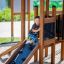 Child playing on Knight's Castle Nature playhouse with slide.
