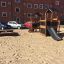 Knight's Castle Nature playhouse with slide in a sandy playground area with a brick apartment buildi