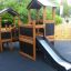 Tower Nature wooden playhouse with slide in a playground setting.