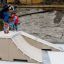 Skateboarder performing a trick on the Bank ramps with a child watching.