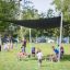 Children playing around a Square bench and table set in a park under a shade structure.