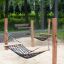 Two Hammock net swings mounted on wooden poles in a sandy playground area in a park.