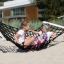 Two children playing on a black net hammock in a sandy outdoor area.