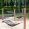 Two Hammock net swings mounted on wooden poles in a sandy playground area in a park.