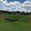 Hammock in a park with wooden posts and a grassy hill in the background.