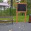 Park bench, blackboard, and trash can set in a park area.