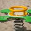 Green and yellow Clover rocking playground equipment on sandy ground
