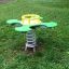 Green Clover rocking toy on a spring in a grassy playground.