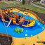Bounty ship with slide in a colorful playground area, fenced and surrounded by buildings.