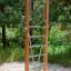 Vertical wooden ladder in a playground surrounded by trees.