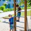 Children playing on a vertical wooden ladder in a playground.