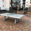 Concrete table tennis, free-standing on a paved courtyard with benches in the background