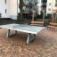 Concrete table tennis, free-standing on a paved courtyard with benches in the background