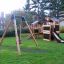 Wooden Swing Frame (single swing) in a playground with climbing structure and slide.