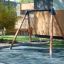 Single swing frame with a wide seat on a playground.