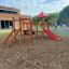 Lemur single slide wooden playground structure with red slide and climbing elements in a park settin